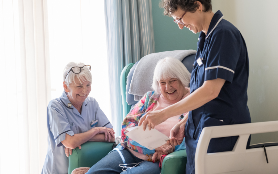 IPU A female patient sitting in a chair, looking at a celebration card with two nurses.