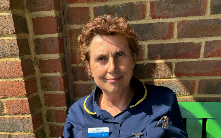 Melica, Registered Nurse Team Leader sat on a green bench outside in the Hospice grounds.